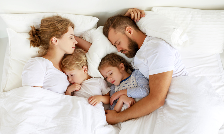 Happy family parents and children sleeping in white bed at home